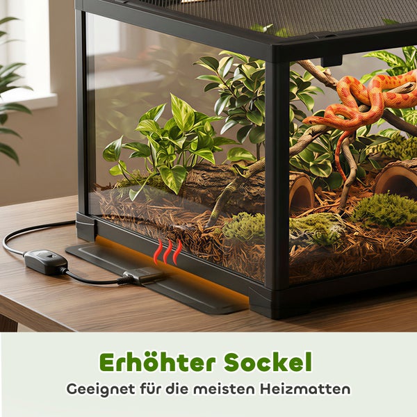 Eingerichtetes Glasterrarium mit schwarzem Rahmen und erhöhtem Sockel für Heizmatten auf einem Holztisch, inklusive Schlange und Pflanzen.