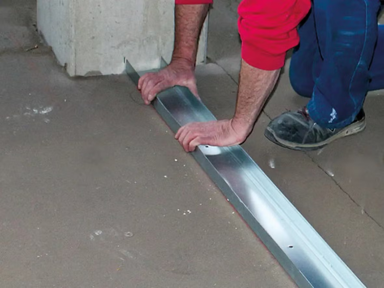 Handwerker positioniert ein Metall U Profil als Bodenprofil für eine Ständerwand auf einem Betonboden
