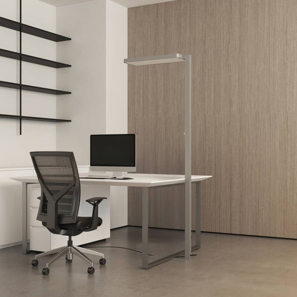 Helle Stehleuchte neben einem Schreibtisch im modernen Büro mit Bürostuhl und Monitor vor einer Holzwand.