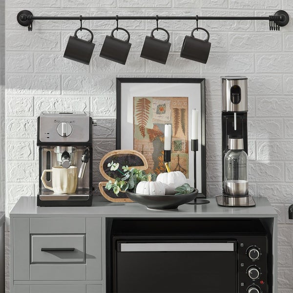 Küchenszene mit Espressomaschine, Wassersprudler, Mikrowelle, Dekoartikeln und Hängeleiste mit Tassen.