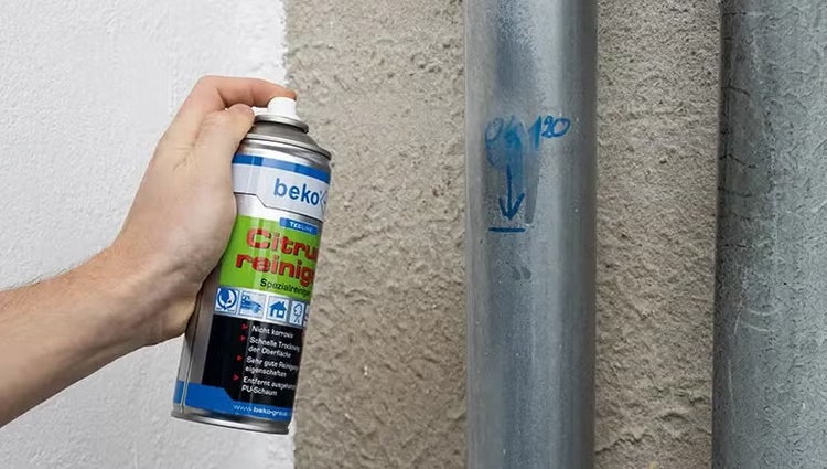 Hand sprüht beko Citrusreiniger auf ein Metallrohr, um blaue Markierungen zu entfernen.