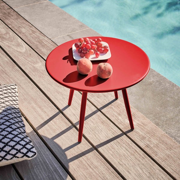 Roter runder Beistelltisch aus Metall auf einer Holzterrasse neben einem Pool mit Obst auf der Tischplatte.