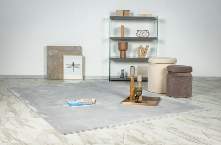 Ein moderner Wohnraum mit einem rechteckigen Teppich auf einem hellen Fliesenboden, ergänzt durch ein Metallregal, zwei Sitzhocker und Dekoration.