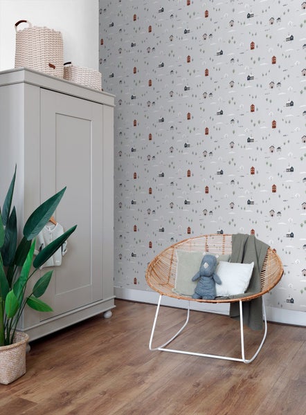 Helles Kinderzimmer mit Vliestapete im Häuser-Design, grauem Kleiderschrank, Rattanstuhl und Holzboden für eine gemütliche Atmosphäre.