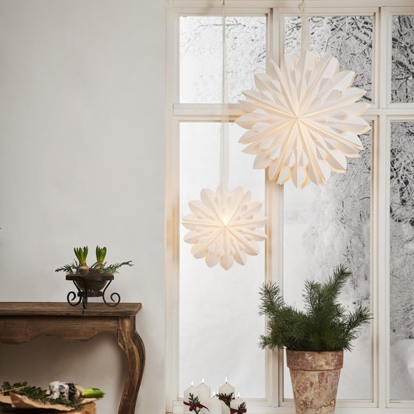 Dekorative Szene mit Papiersternen am Fenster, Pflanzen auf einem Holztisch und Kerzen