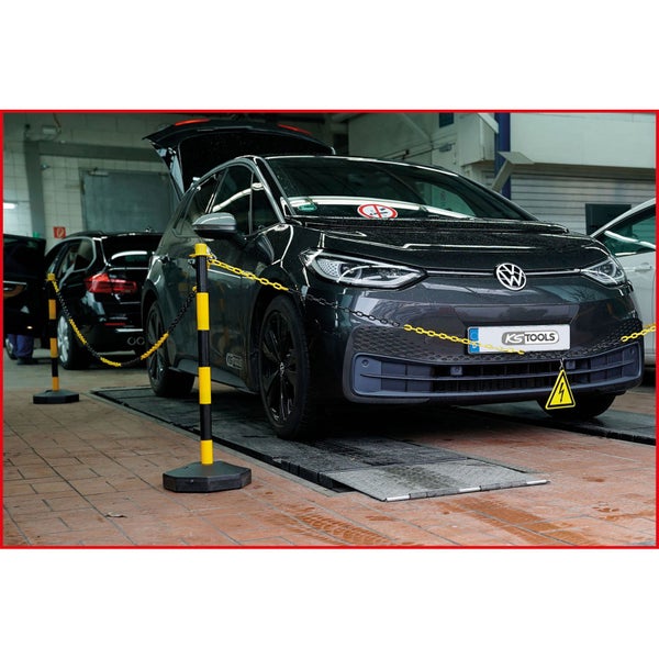Eine Werkstattszene mit einem Elektroauto auf einer Hebebühne, abgesperrt mit Kettenständern.