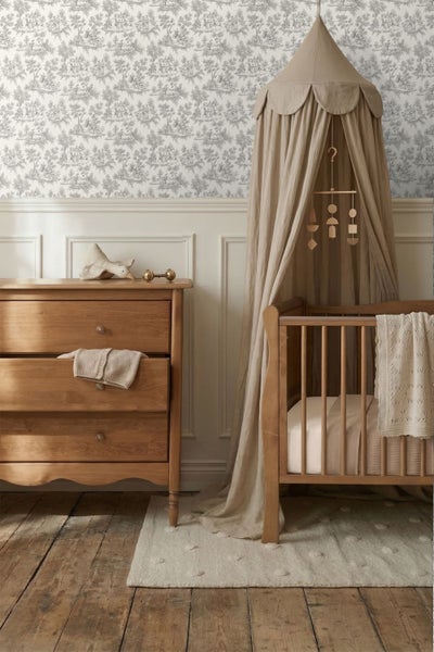 Vliestapete mit Toile-de-Jouy-Muster in einem hellen Kinderzimmer mit klassischen Holzmöbeln und Betthimmel über dem Gitterbett.