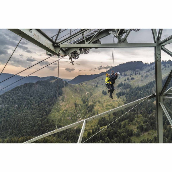 Zwei Personen bei der Höhenarbeit mit Absturzsicherung an einer Metallkonstruktion vor einer Berglandschaft.