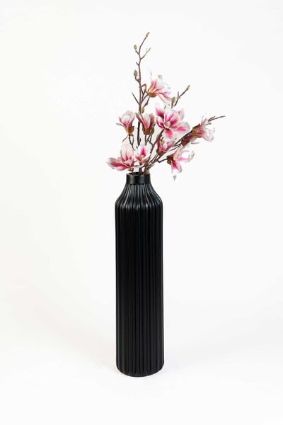Schwarze hohe Vase mit vertikaler Rillenstruktur und künstlichen Magnolienblüten.