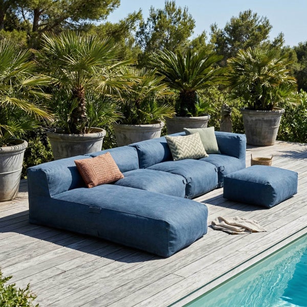 Modulares blaues Outdoor-Lounge-Sofa mit Hocker und Kissen auf einer hellen Holzterrasse am Pool, umgeben von Palmen.
