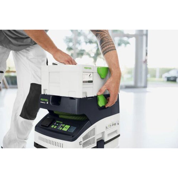 Handwerker befestigt einen weißen Festool Systainer auf einem Festool Absaugmobil in einer hellen, organisierten Werkstatt.