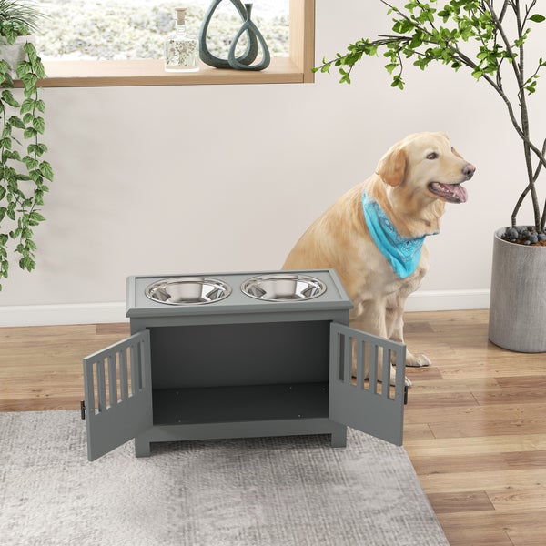 Graue Hunde-Futterstation aus Holz mit zwei Edelstahlnäpfen und Unterschrank mit Türen, neben einem sitzenden Hund im Wohnraum.