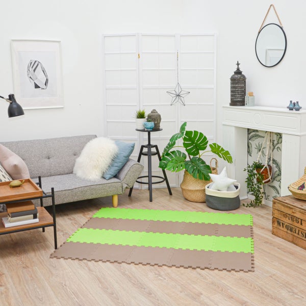 Helles Wohnzimmer mit grauem Sofa, Holzmöbeln und einer grün-braunen Puzzlematte auf einem Boden in Holzoptik.