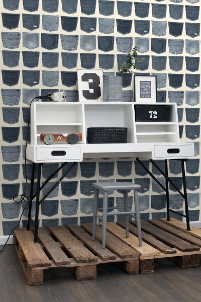 Szene mit Schreibtisch, Hocker und einer Wand mit Jeanshosentaschen-Motiv.
