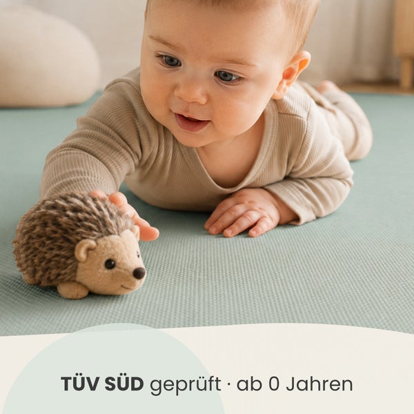 Ein Baby spielt auf einer Spielmatte mit einem Plüschigel der TÜV SÜD geprüft und für Kinder ab null Jahren geeignet ist.