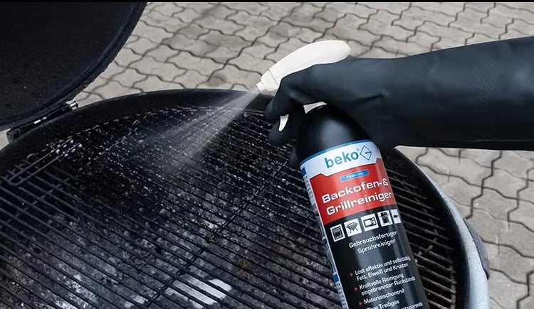 Hand mit Schutzhandschuh sprüht beko Backofen- und Grillreiniger auf einen verschmutzten Grillrost.