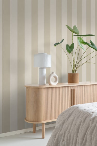 Wohnraum mit gestreifter Tapete, Kommode, Lampe und Zimmerpflanze.