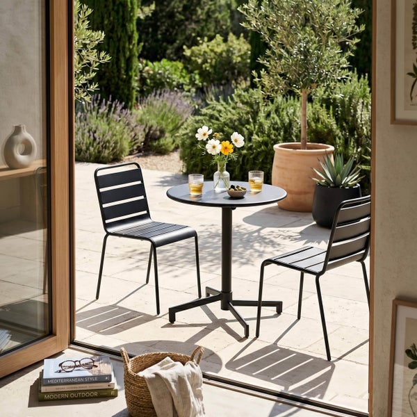 Schwarzes Gartenmöbel-Set bestehend aus einem runden Bistrotisch und zwei Metallstühlen auf einer sonnigen Terrasse mit mediterranem Flair.