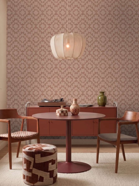 Wohnzimmer mit geometrisch gemusterter Tapete, einem runden Tisch, zwei Holzstühlen, einem Pouf und einer modernen Hängeleuchte.