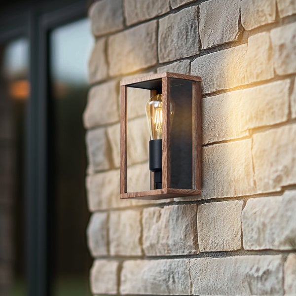Moderne Außenwandleuchte mit Holzrahmen und Glaseinsätzen, montiert an einer Steinwand, mit leuchtendem Filament-Leuchtmittel.