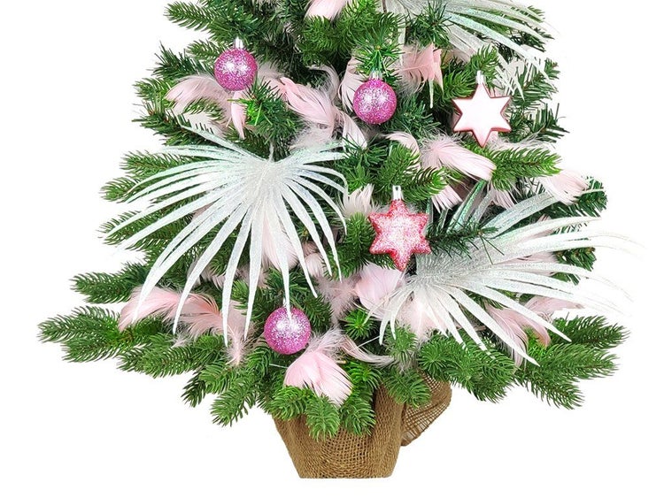Weihnachtsbaum im Topf dekoriert mit Christbaumkugeln, Sternen, Federn und künstlichen Palmenblättern in einem Jutesack.