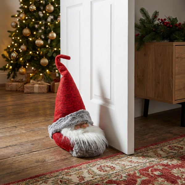 Weihnachts Türstopper in Wichteloptik mit langer Mütze und Bart vor einer weißen Tür in einem weihnachtlich geschmückten Raum.