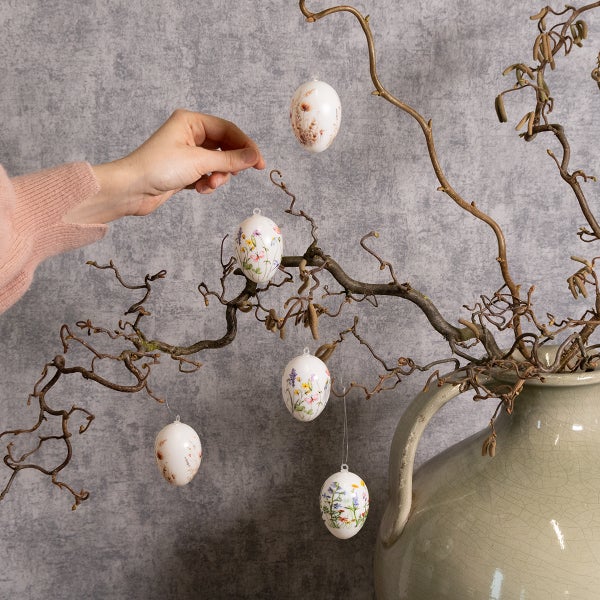 Dekorierte Ostereier hängen an einem Zweig in einer Vase, verziert mit Blumenmustern