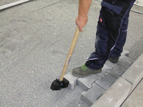 Eine Person verlegt Pflastersteine mit einem Gummihammer auf einem Untergrund.