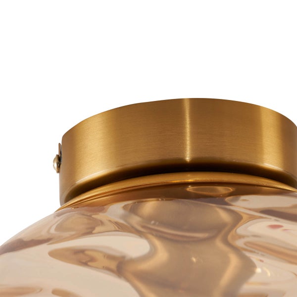 Detailaufnahme einer Deckenleuchte mit goldfarbener Halterung und gewelltem Glasschirm