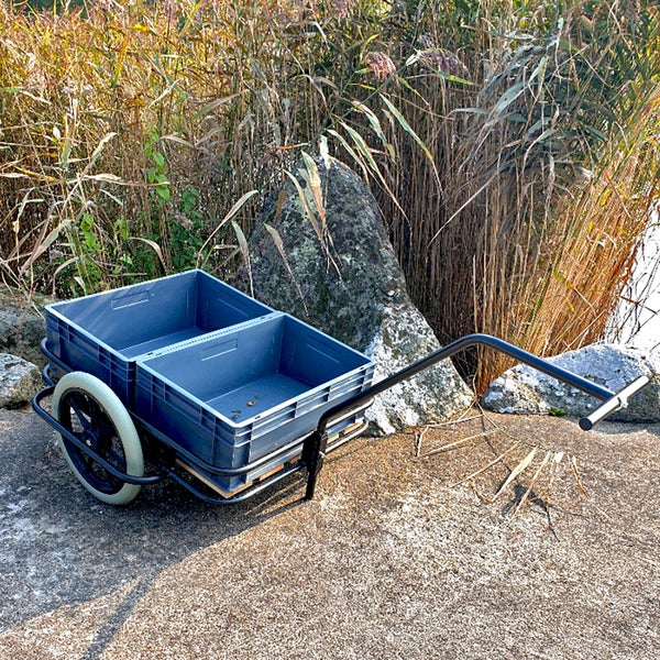 Handwagen mit zwei Kunststoffkisten und großen Rädern auf befestigtem Boden im Außenbereich.