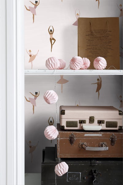 Dekorative Szene mit Tapete mit Ballerina-Motiv, einer Lichterkette mit rosa Papierkugeln und gestapelten Koffern