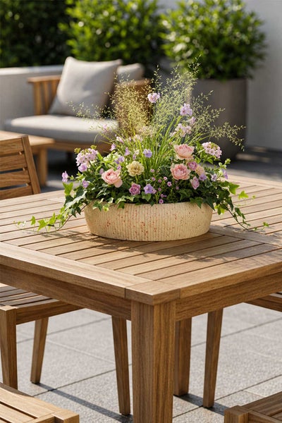Helle Terrasse mit Gartenmöbeln aus Holz und einer runden Pflanzschale mit Blumen auf dem Tisch.