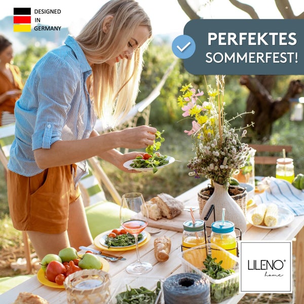Eine Frau deckt einen Gartentisch für ein Sommerfest im Freien mit Tellern, Gläsern, Blumen und Kissen von LILENO home.