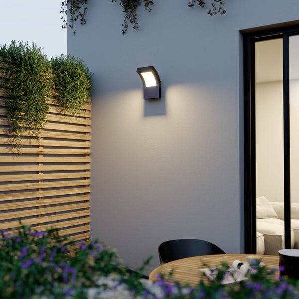 Moderne LED-Außenwandleuchte an einer Hauswand auf einer Terrasse mit Holzlamellenzaun und Gartenmöbeln.