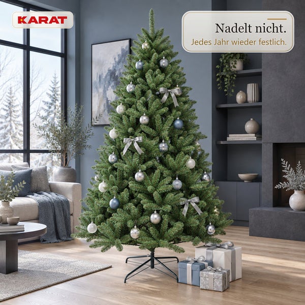 Künstlicher Weihnachtsbaum von Karat, festlich geschmückt mit Kugeln und Schleifen, nadelfrei, steht in einem modern eingerichteten Wohnzimmer.