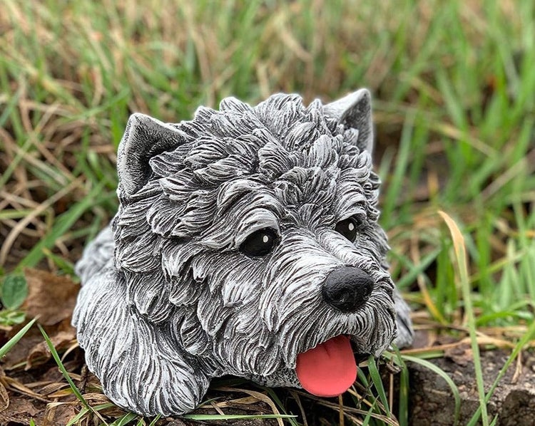 Gartenfigur in Form eines Hundes aus Steinguss, grau-weiß strukturiert, mit heraushängender Zunge, platziert im Gras.