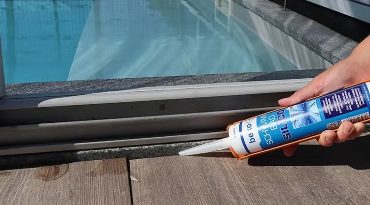 Hand appliziert beko Schwimmbad Silikon an der Fuge zwischen Fliesen und Schwimmbeckenrand.