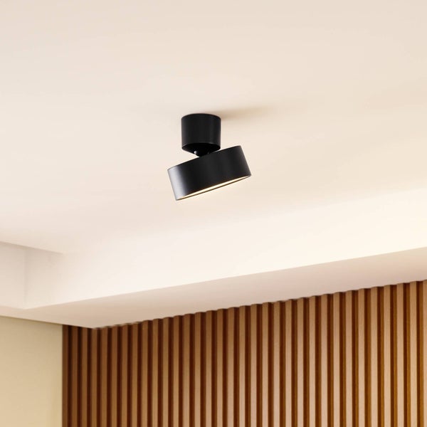 Moderner schwarzer zylindrischer Deckenstrahler mit neigbarem Leuchtenkopf an einer Decke vor einer Holzwand.