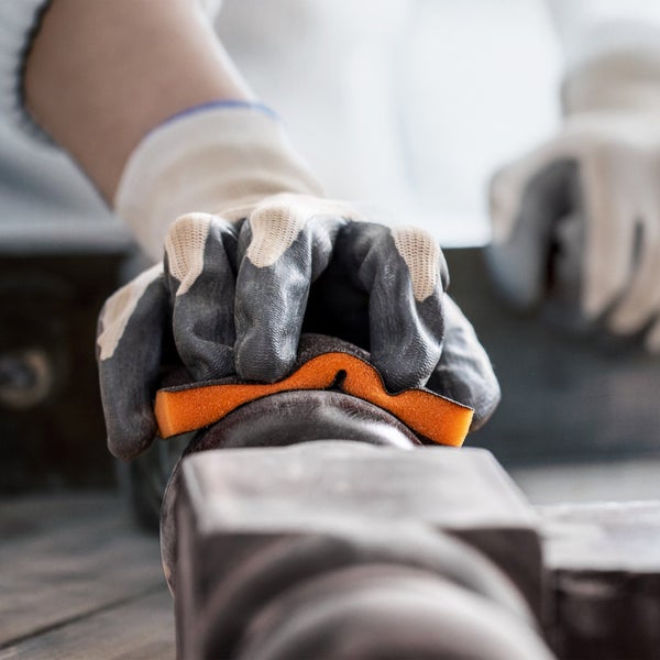 Nahaufnahme einer Person mit Handschuhen, die einen Schleifschwamm auf einem Werkstück verwendet.