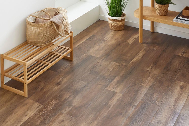 Heller, organisierter Raum mit dunklem Vinylboden in Holzoptik, einem Schuhregal aus Holz, einem geflochtenen Korb und Pflanzen.