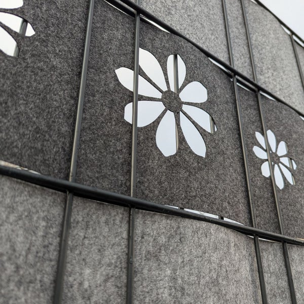 Detailansicht eines grauen Zaunsichtschutzes mit Blumenausschnitten.