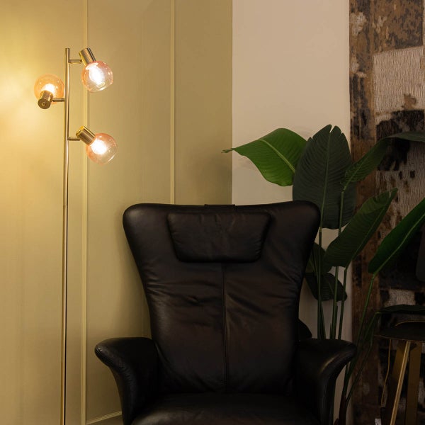 Stehlampe mit drei Leuchten und einem Sessel im Raum.