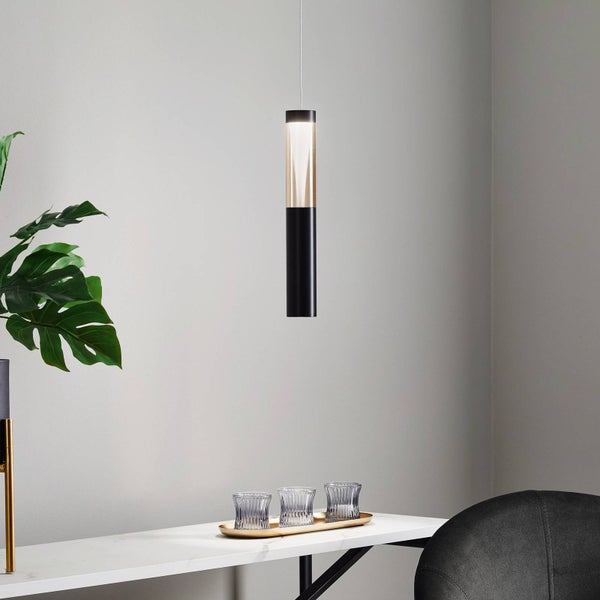 Moderne zylindrische Pendelleuchte über einem weißen Marmortisch mit Monstera-Pflanze und dekorativen Gläsern in einem hellen Raum.