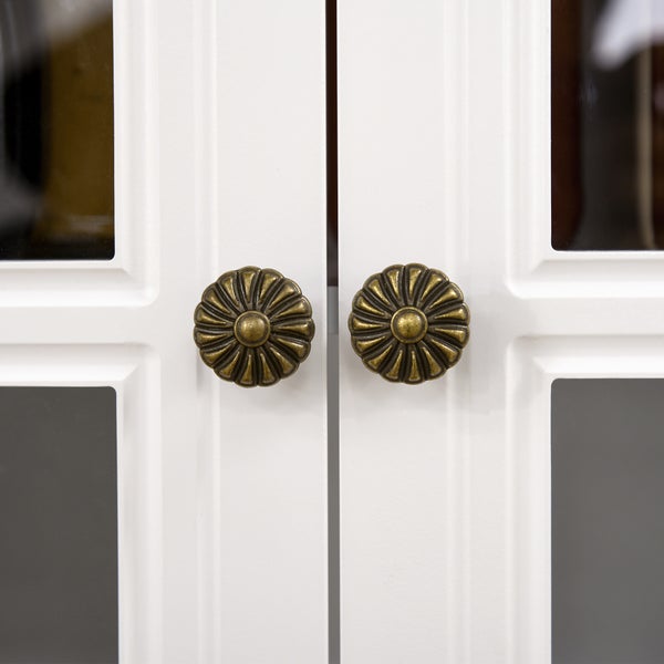 Zwei blumenförmige Möbelknöpfe in Bronze-Optik an weißen Schranktüren mit Glaseinsätzen.