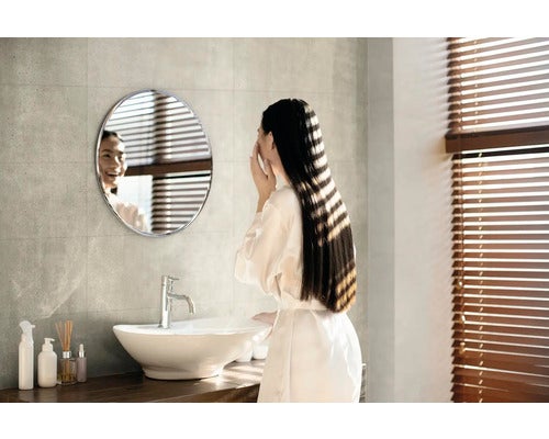 Helles Badezimmer mit rundem Spiegel, Waschbecken und Frau vor dem Spiegel
