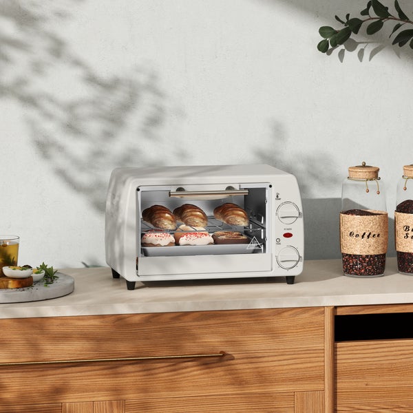 Weißer Minibackofen auf einer hellen Küchenarbeitsplatte aus Holz, gefüllt mit Croissants und Gebäck.