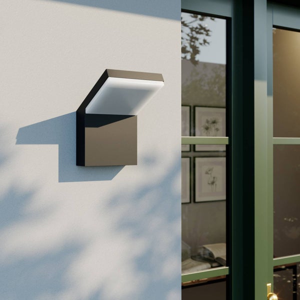 Moderne LED-Außenwandleuchte in Anthrazit mit weißem Diffusor an einer hellen Hauswand neben einer Glastür.