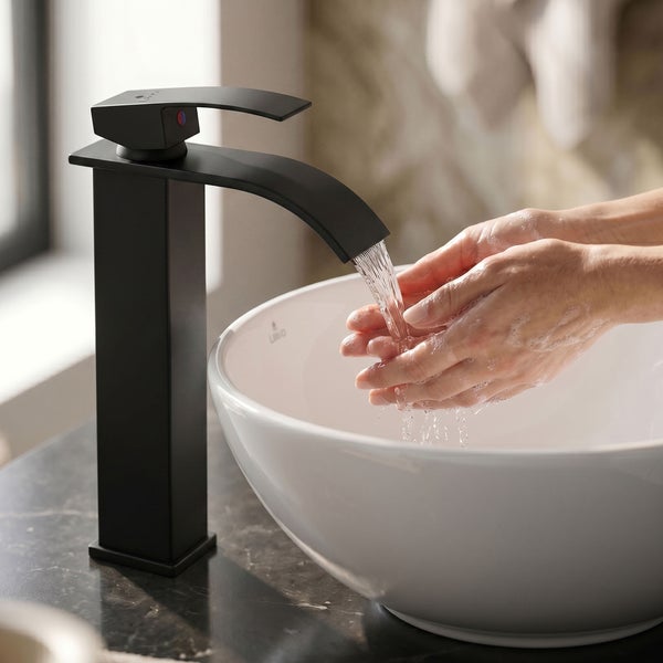 Schwarze Waschtischarmatur mit Wasserfall-Auslauf an einem weißen Aufsatzwaschbecken während der Nutzung.