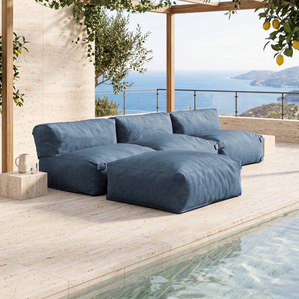 Modulare Outdoor-Lounge in Blau auf einer hellen Steinterrasse mit Pool und Blick auf das Meer.