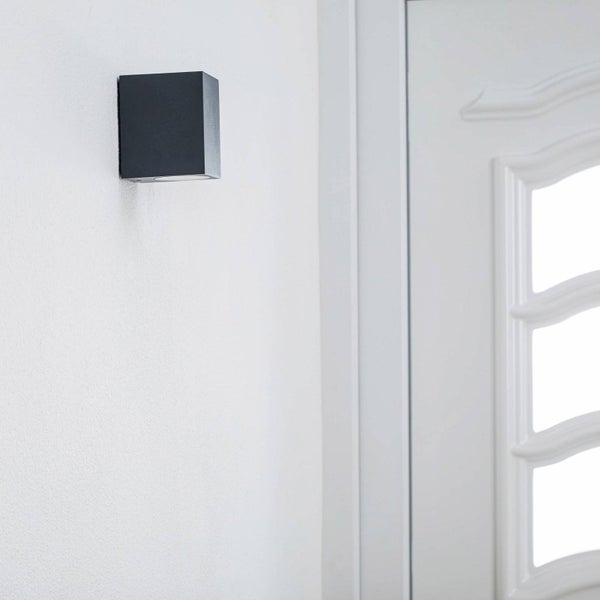 Würfelförmige Wandleuchte im modernen Design montiert an einer Wand neben einer Haustür.